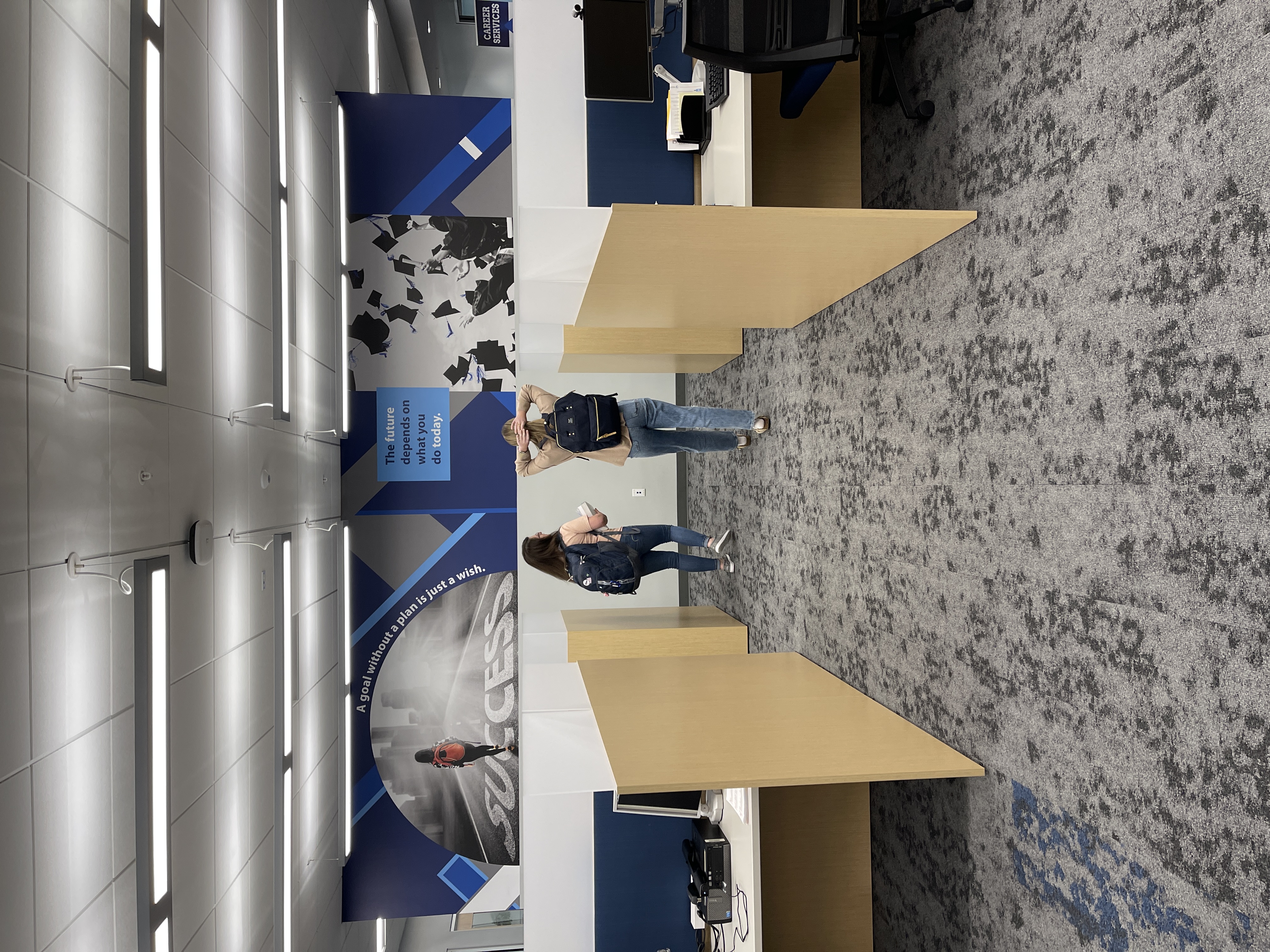 two students walking in between desks at student success center